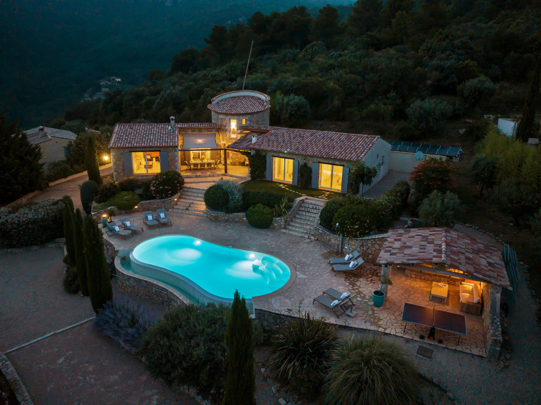 Luftaufnahme der Ferienvilla La Genestière in Seillans mit beleuchtetem Infinity-Pool bei Abendstimmung in Südfrankreich